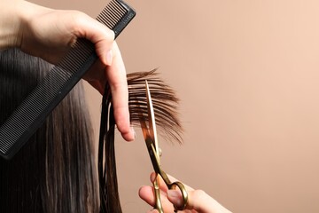 Hairdresser cutting client's hair with scissors on light brown background, closeup. Space for text