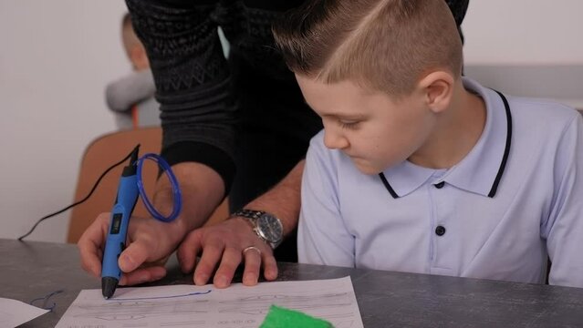 A close-up of a teacher teaching a little boy to work at a robotics school with a 3d pen. Computer class in a modern school.