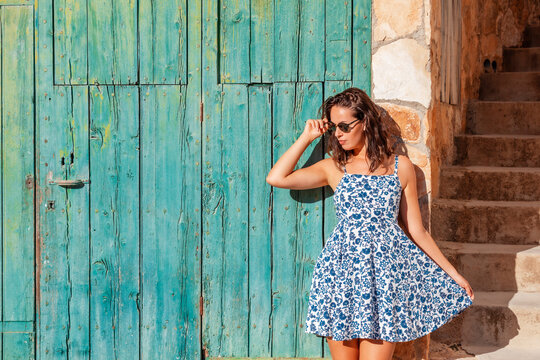 young brunette woman standing near a door wearing a blue and white floral pattern dress 