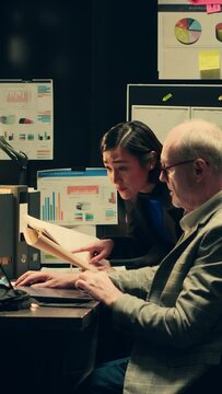 Vertical Video Law agents studying old classified information from police archives folders, looking for clues and crime trends. Partners accessing additional archived resources in incident room