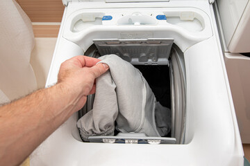 A man puts clothes in the drum of a washing machine.