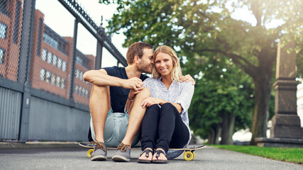 a young couple sits outdoors on a skateboard and smiles into the camera - 740676240