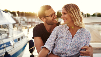 A smiling man looks in love at his girlfriend as they sit on a boat and enjoy the sunset - 740676264