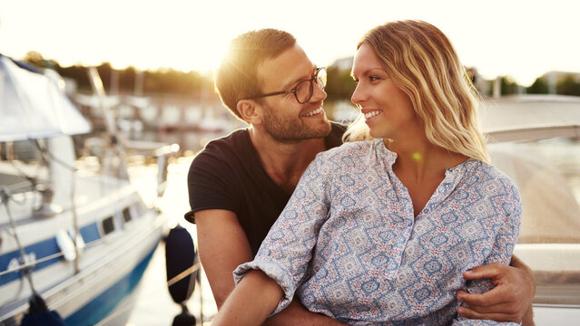 A smiling man looks in love at his girlfriend as they sit on a boat and enjoy the sunset