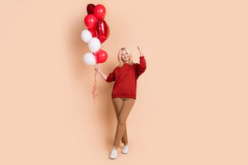 Full length photo of lucky funky woman wear red sweater rising fist holding balloons bunch isolated...