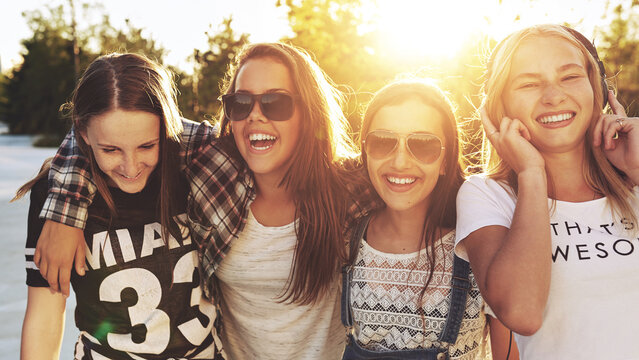 Teenage girls laughing wearing sunglasses and headphones outdoors in the sunset