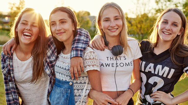 A group of smiling teenage girls stand side by side with earphones around their necks