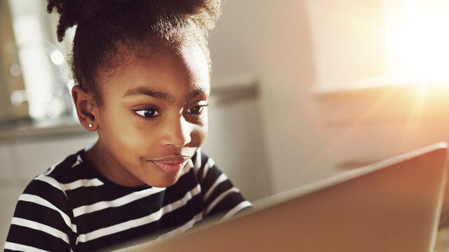 Focused smiling little black girl sitting and watching something on her laptop at home