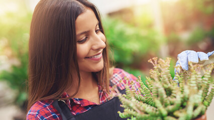 Smiling young female gardener stands in a nursery and arranges plants