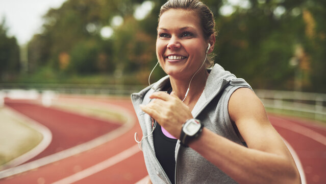 Young smiling woman running on stadium with a pulse watch on the wrist