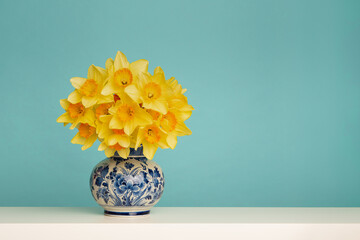 Bouquet of daffodil flowers in a delft blue vase on a blue background