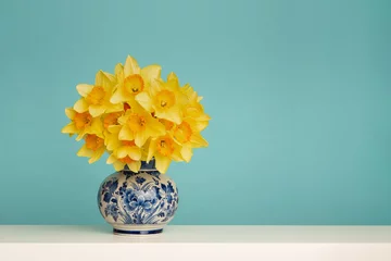 Poster Im Rahmen Bouquet of daffodil flowers in a delft blue vase on a blue background © Elles Rijsdijk