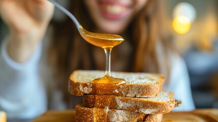 Young woman holding a spoon, spreading the sweet honey on a homemade whole grain wheat cereal bread slices on the wooden board on the kitchen table. Organic foods' dessert meal, delicious breakfast