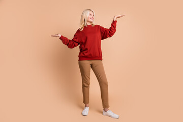 Full length photo of funny confident lady dressed red pullover showing arms scales looking empty space isolated beige color background
