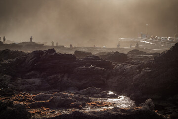 Rocks in the foreground, with people enjoying an end-of-day walk on the beach