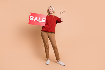 Full length photo of excited funky woman wear red sweater rising sale billboard isolated beige color background