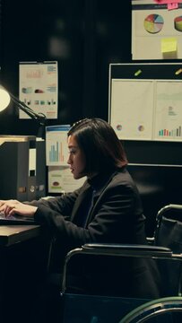 Vertical Video Wheelchair user and inspector analyzing criminal records in police archive room, cross reference data from cases to identify similarities. Team of agents compile notes on crime trends
