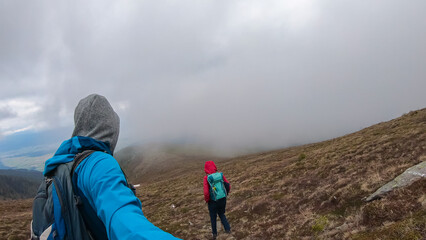 Hiker couple walking on alpine meadow through thick fog near mountain peak Hornischegg, Mur Valley,...