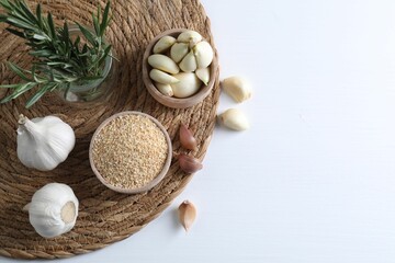 Dehydrated garlic granules in bowl, rosemary and fresh cloves on white table, flat lay. Space for text
