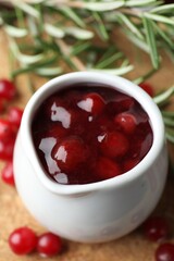 Cranberry sauce in pitcher, fresh berries and rosemary on board, closeup