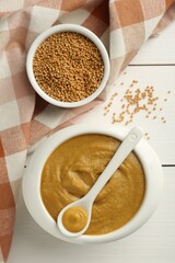 Tasty mustard sauce and dry seeds on white wooden table, flat lay