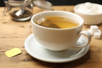 Tea brewing. White cup with tea bag on wooden table, closeup