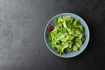 Green salad leaves in bowl on black table.