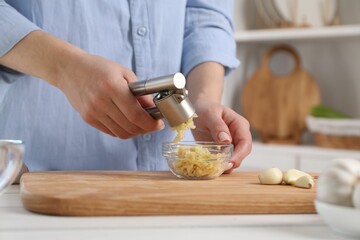 Woman squeezing garlic with press at white table in kitchen, closeup - obrazy, fototapety, plakaty