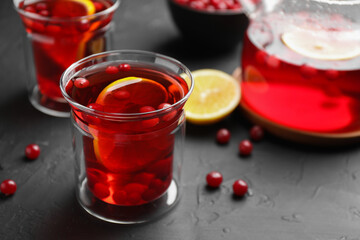 Tasty hot cranberry tea with lemon and fresh berries in glass on black textured table