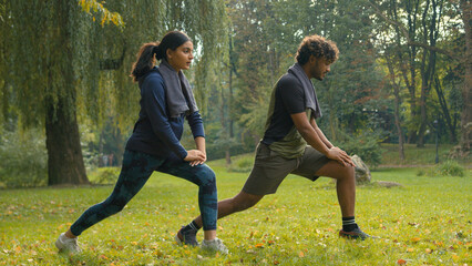 Confident determined Indian couple Arabian man woman girl guy doing lunges squats exercises sport morning workout in park outdoors fit friends people team sports body weight training personal coach