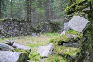 Fototapeta na wymiar Close up view of stone ruins of medieval building in dense forest in Mur Valley, Lavanttal Alps, Styria, Austria. Misty atmosphere in remote Austrian Alps. Decayed walls are overgrown with green moss