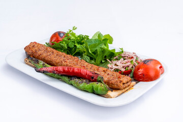 Top view of traditional grilled Adana kebab with cooked spicy shish kebab, pepper, tomato, and fresh greenery on a white plate isolated on white background.