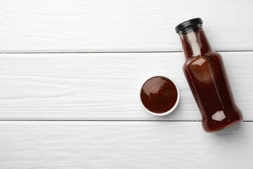 Tasty barbeque sauce in bottle and bowl on white wooden table, top view. Space for text