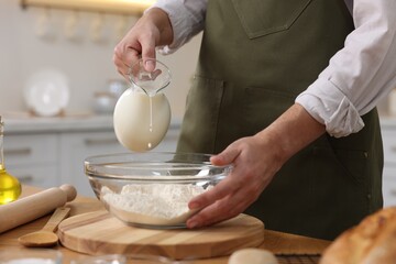 Making bread. Man pouring milk into bowl with flour at wooden table in kitchen, closeup