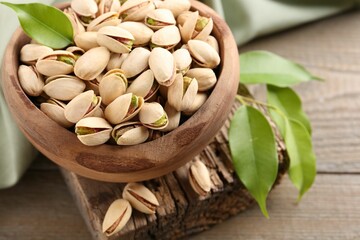 Delicious pistachios in bowl on wooden table, closeup