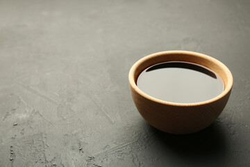 Soy sauce in wooden bowl on black textured table. Space for text