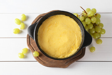Fondue with tasty melted cheese and grapes on white wooden table, flat lay