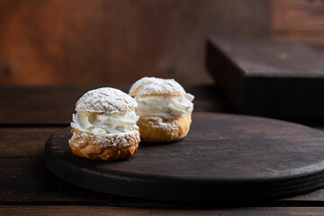 Profiteroles cakes with butter cream on a wooden dark background