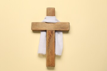 Wooden cross and white cloth on beige background, top view. Easter attributes