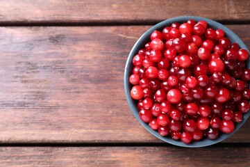 Fresh ripe cranberries in bowl on wooden table, top view. Space for text