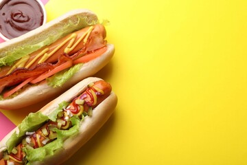 Delicious hot dogs with lettuce and sauces on yellow background, flat lay. Space for text