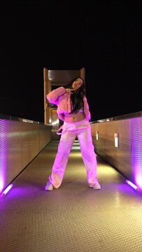 Low angle view of a happy trap dancer in pink clothes dancing alone outdoors at night