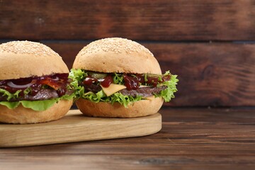 Board with delicious cheeseburgers on wooden table, closeup. Space for text