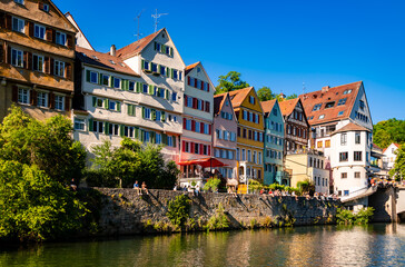 Neckarfront panorama in Tuebingen in Baden-Wuerttemberg Germany on a sunny summer day with colorful renovated facades. People relaxing and chilling on a popular old brick wall above river Neckar. - obrazy, fototapety, plakaty