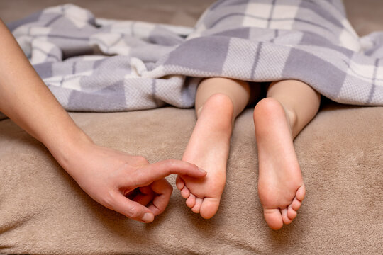 Children's feet under a blanket are tickled by their mother's hand