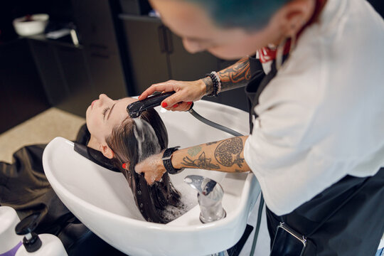 Creative female hairdresser is washing hair of young woman in beauty salon. High quality photo