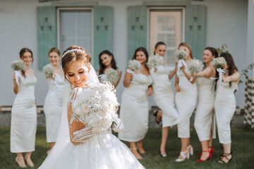 The bride in a long wedding dress with a veil poses in front of her friends in white dresses
