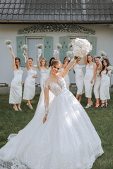 The bride in a long wedding dress with a veil poses in front of her friends in white dresses