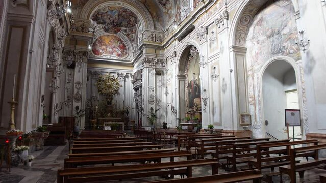 Gimbal footage over wooden pew chairs towards imposing altar in beautifully decorated San Benedetto church in Catania, Italy

