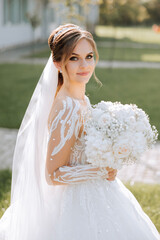 Portrait. A brunette bride in a dress and a veil, with a diadem, poses with a bouquet. Silver...